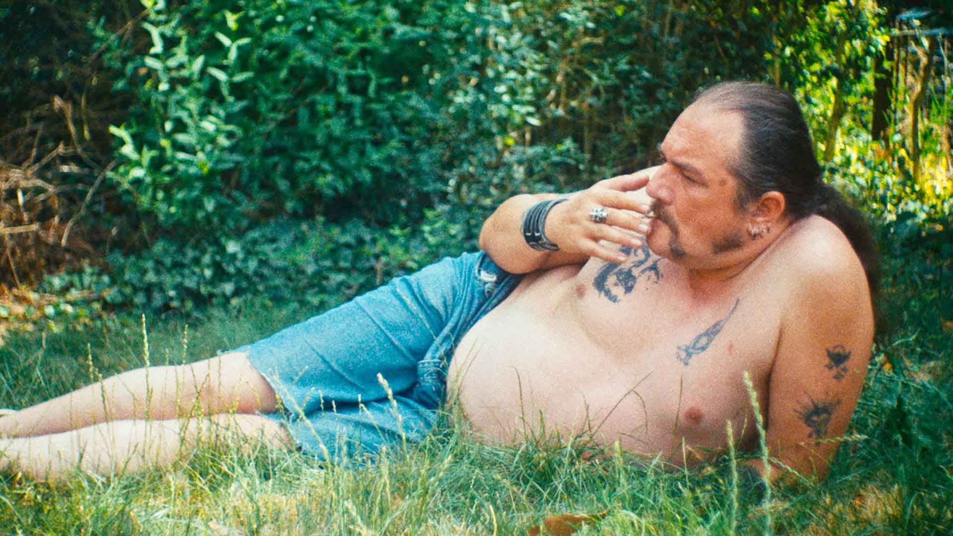 Un homme cinquantenaire fume torse nu dans l'herbe