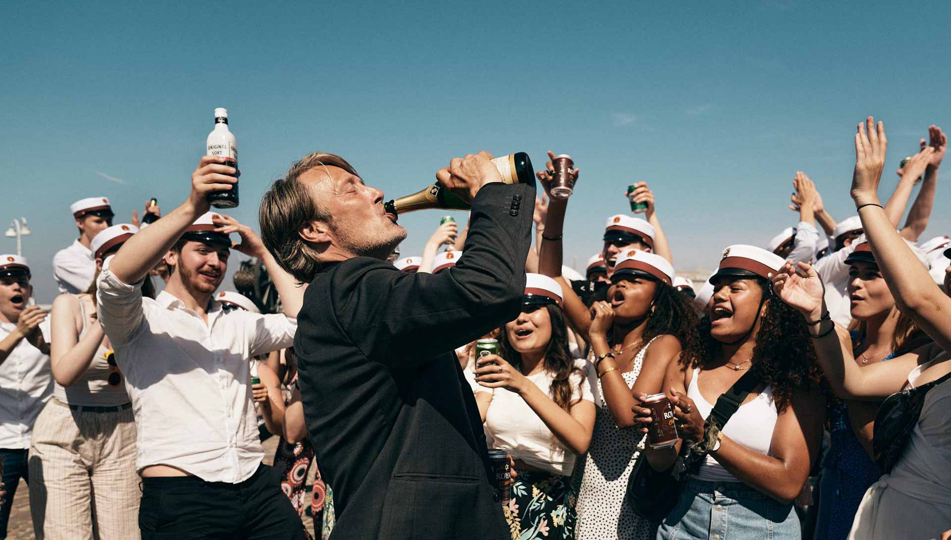 Photo d'une fête. En premier plan, un homme boit une bouteille. Extrait du film Drunk de Thomas Vinterberg