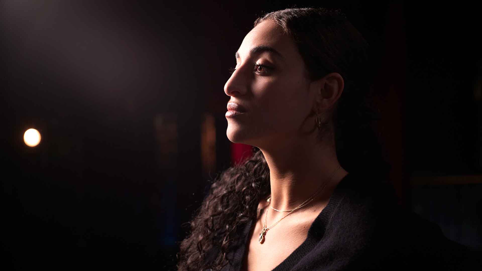 Une jeune femme, de profil, regarde au loin. Elle est dans le clair-obscur.