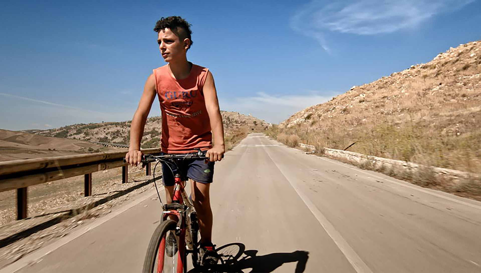 Un jeune garçon fait du vélo sur une route déserte. Extrait du documentaire Il mio corpo de Michele Pennetta