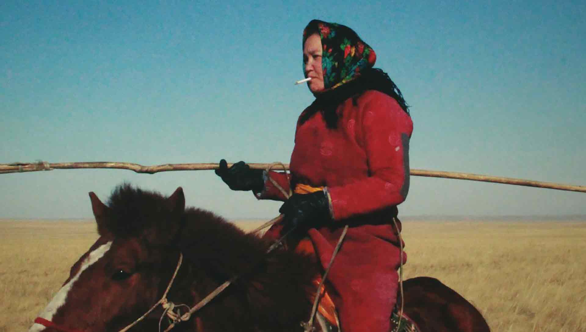 Une femme qui fume une cigarette est à cheval dans la steppe mongole. Extrait du film La femme des steppes, le flic et l’oeuf de Quanan Wang