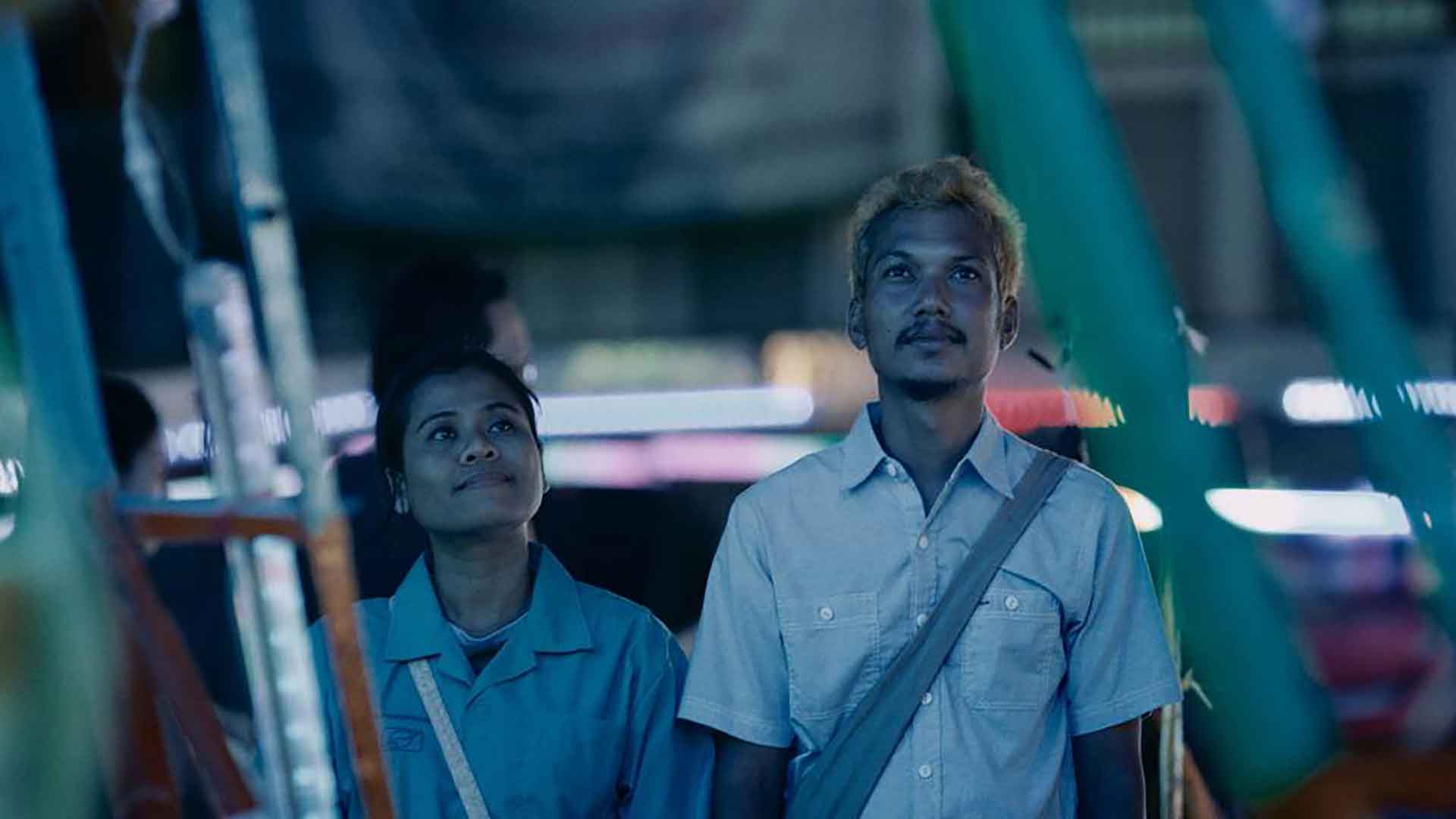 Un homme et une femme sont dans un parc d'attraction le soir et regarde vers le ciel. Extrait du film Manta Ray de Phuttiphong Aroonpheng