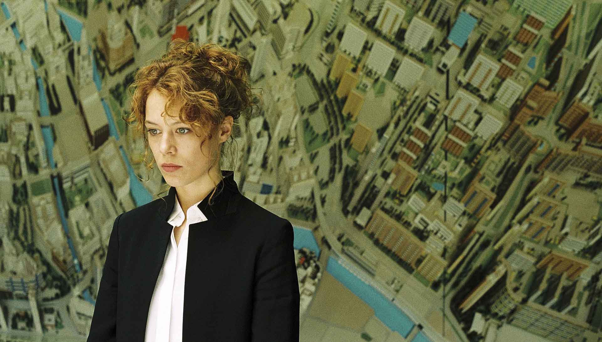 Jeune femme devant un mur représentant la carte d'une ville. Extrait du film Ondine de Christian Petzold.