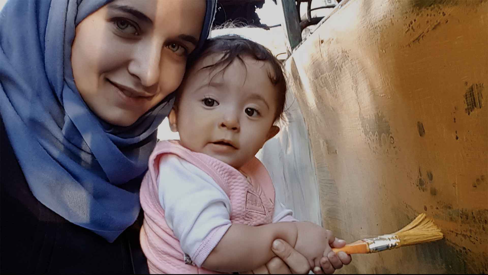 Une Syrienne tient dans ses bras un enfant qui fait de la peinture