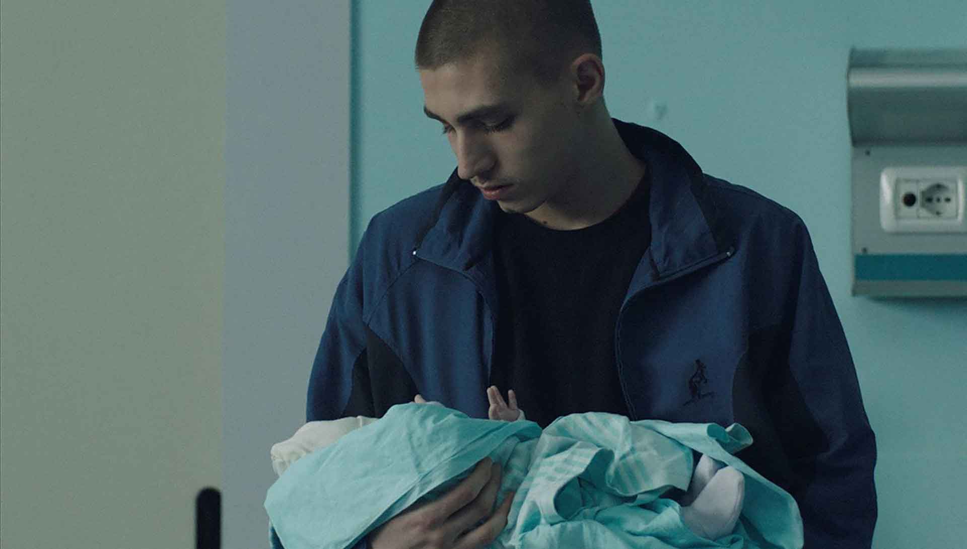 Un jeune homme tient un bébé dans ses bras. Extrait du film Sole de Carlo Sironi