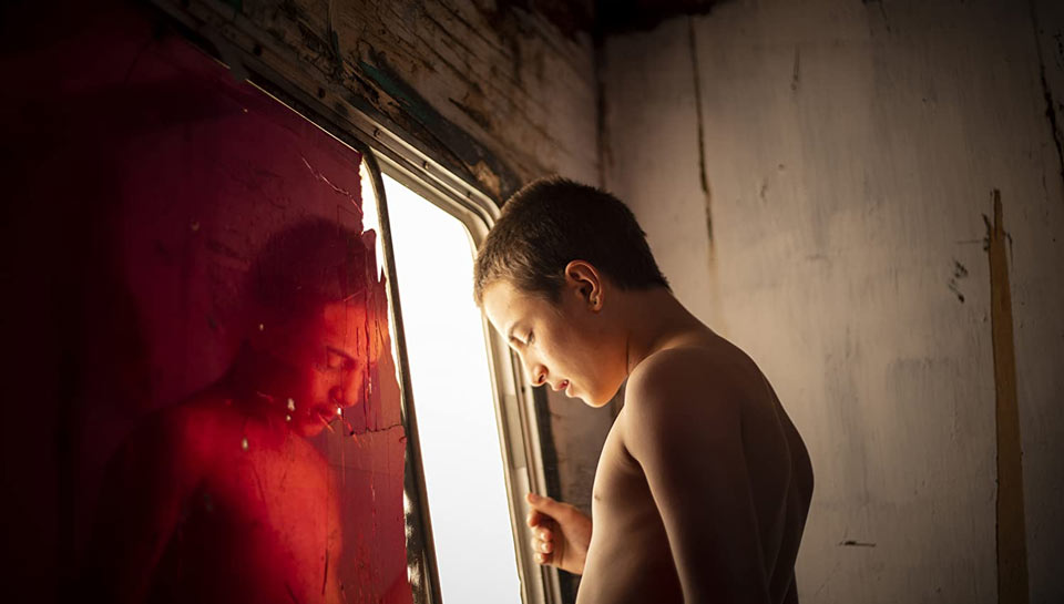 Plan d'un adolescent et son reflet dans une vitre fisurée rouge. Extrait du film 