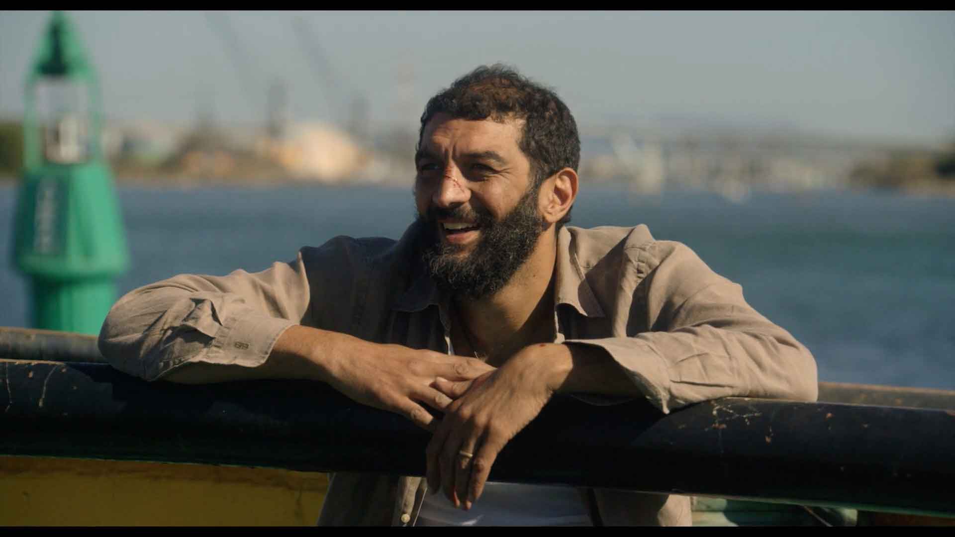 Un homme souriant est adossé sur une barrière près de la mer