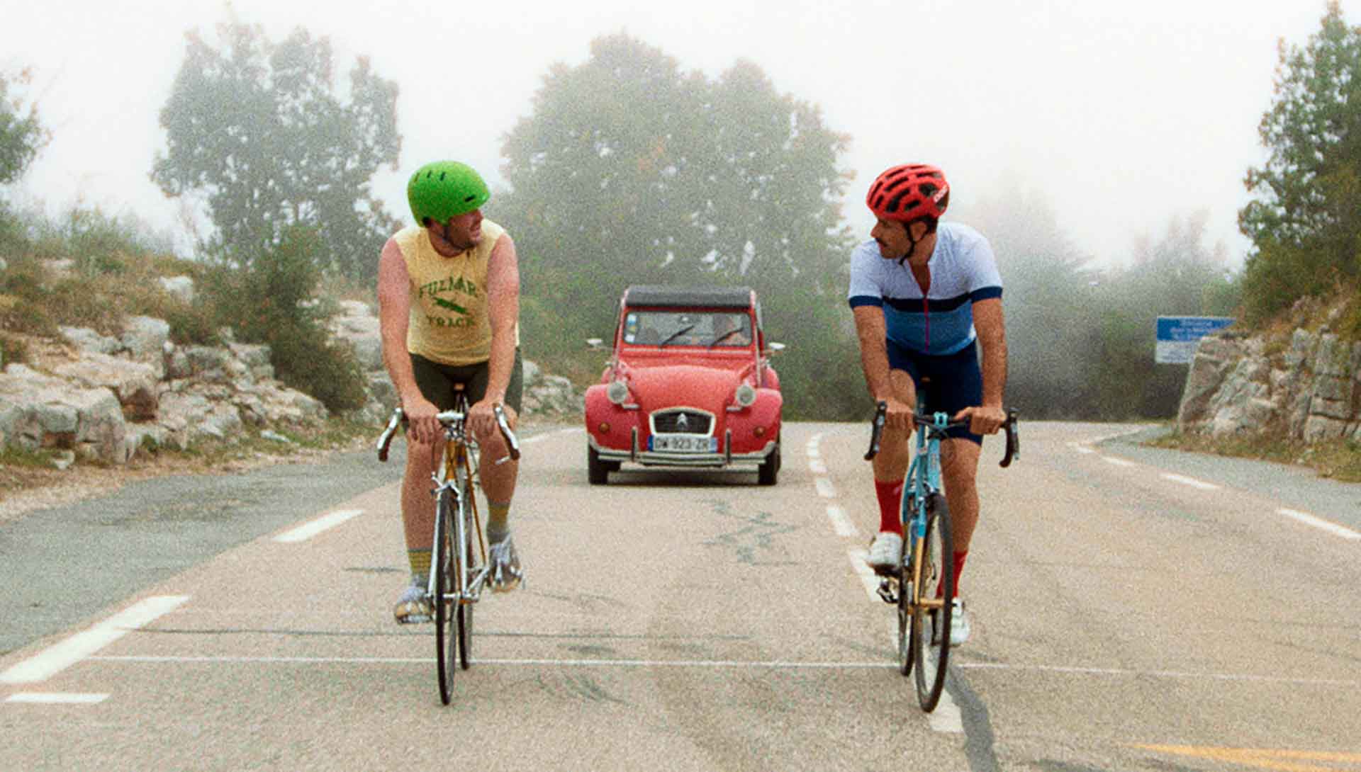 Deux cyclistes pédalent devant une Citroën 2 CV. Extrait du film The Climb de Michael Angelo Covino