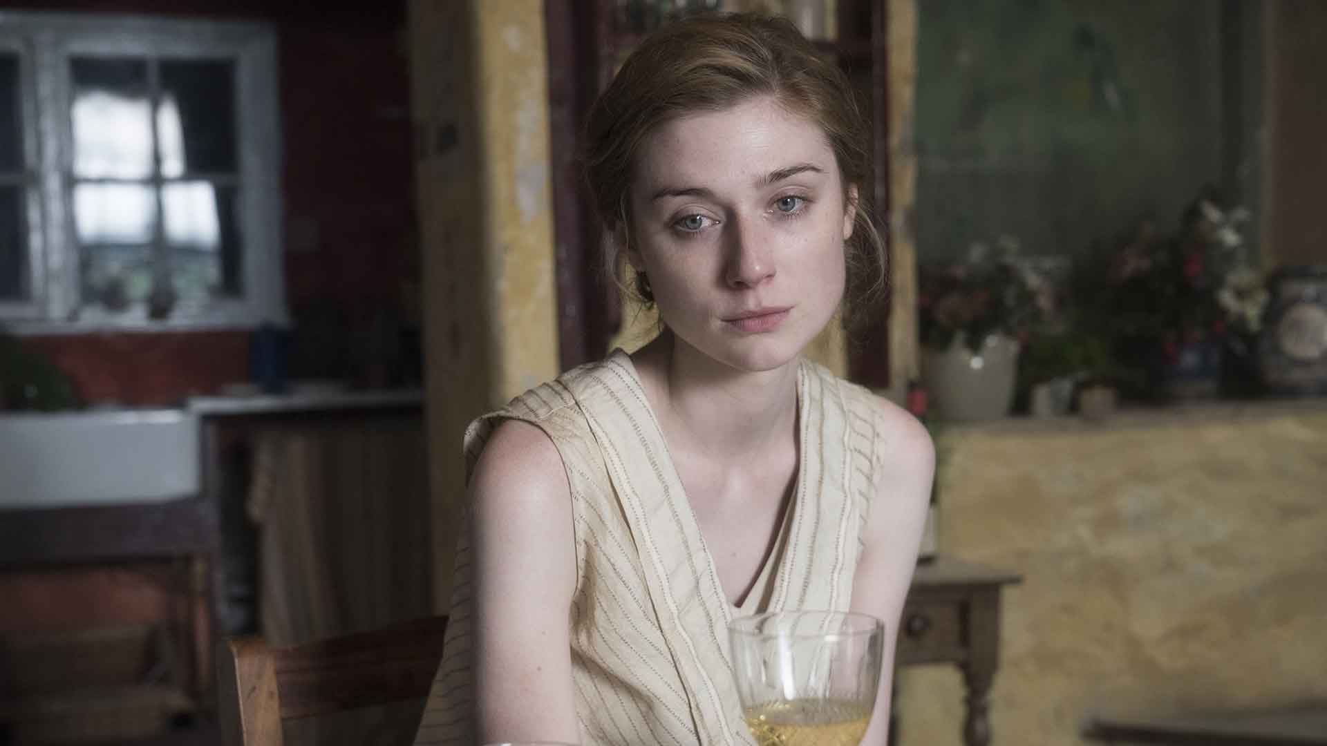 Une jeune femme triste est face caméra devant un verre de vin blanc